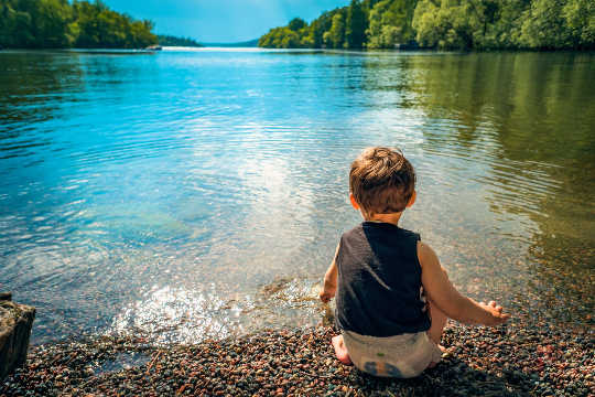young child sitting at the edge of a peaceful lake